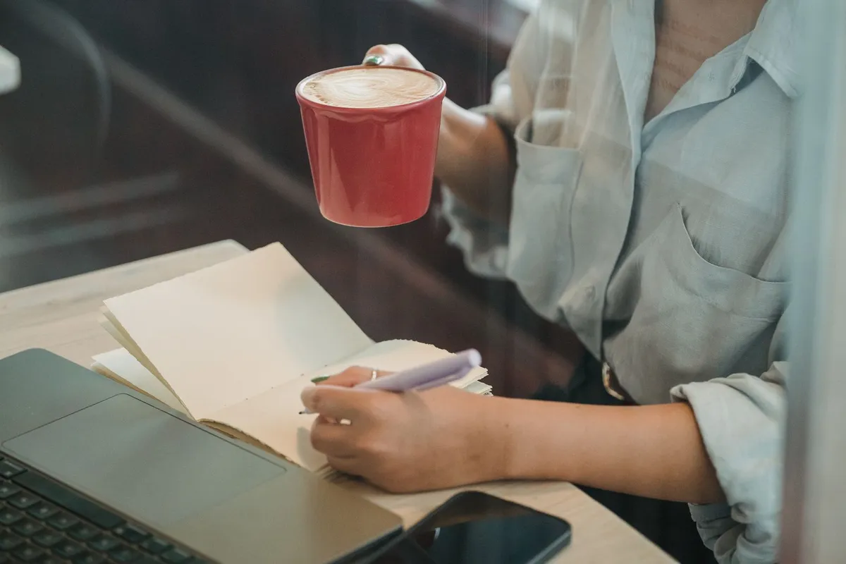 コーヒーを片手にノートに書き込む手元