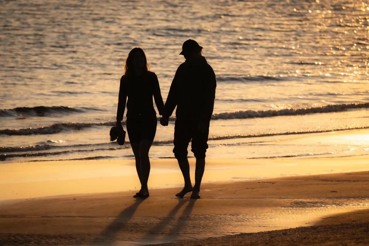 夕暮れの浜辺を手をつないで歩くカップルのシルエット