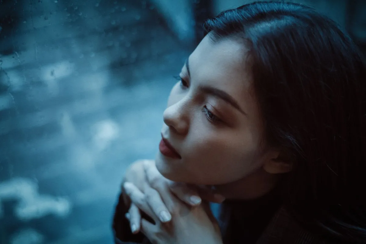 雨の窓辺で物思いにふける女性